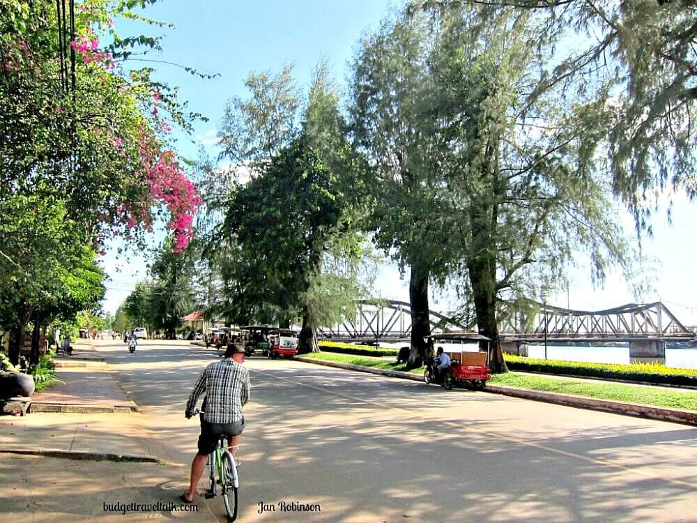 Man on Bicycle on the paves Riverfront Boulevard in Kampot Cambodia with bridge in background