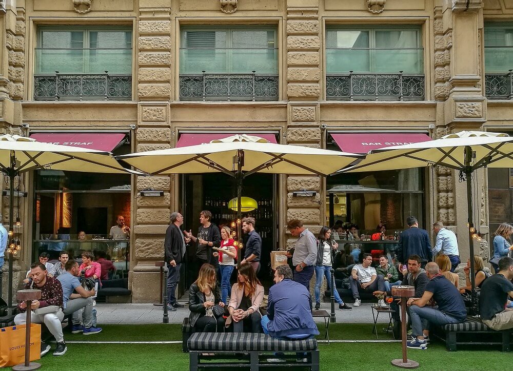 A photo of a bar in Milan Italy at Aperitivo time with people spilling out into the street.